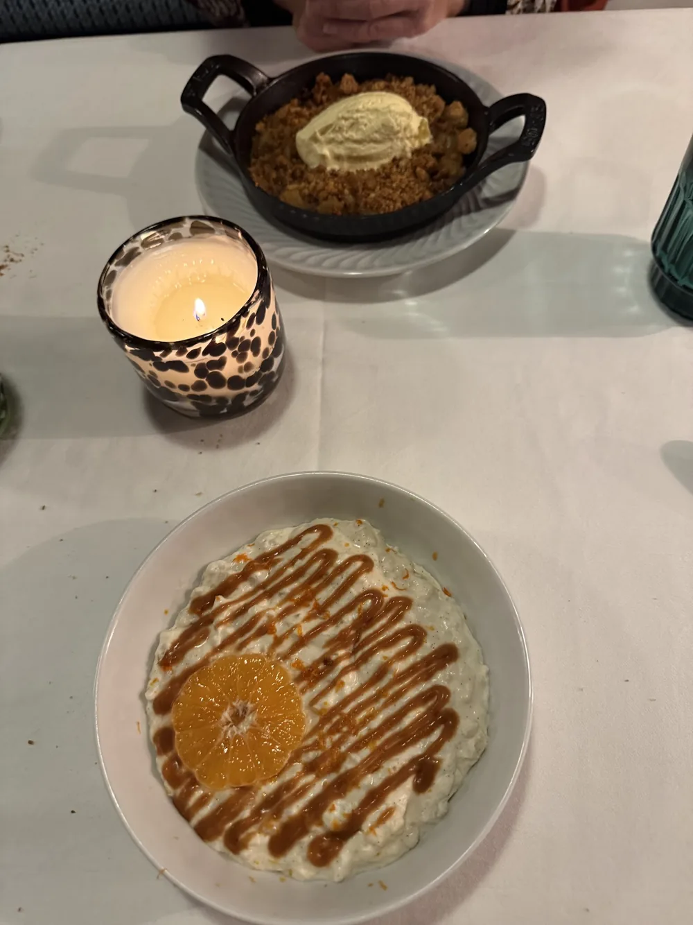 Riz au lait nappé de caramel avec une rondelle d'orange, à côté d'un petit plat noir et d'une bougie