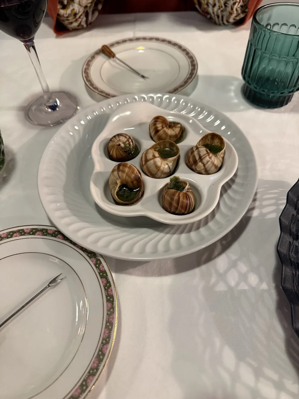 Escargots en coquille servis dans un plat blanc, sur une table dressée avec des verres turquoise