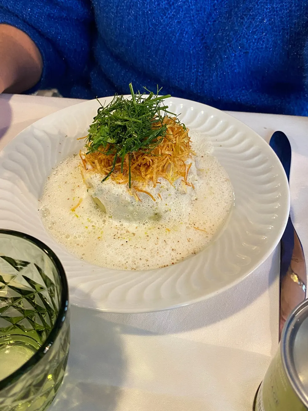 Assiette blanche garnie d'une préparation crémeuse, surmontée de fins filaments croustillants et d'herbes
