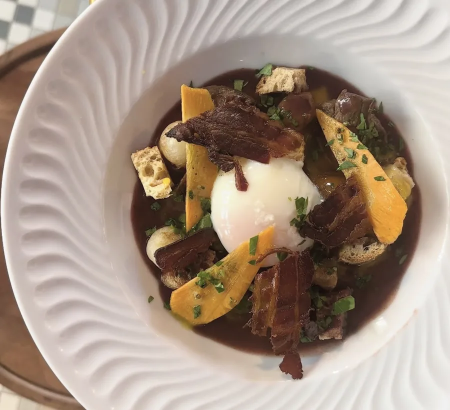 Œuf poché sur de la viande mijotée en sauce brune, avec des lamelles de légumes jaunes et des croûtons