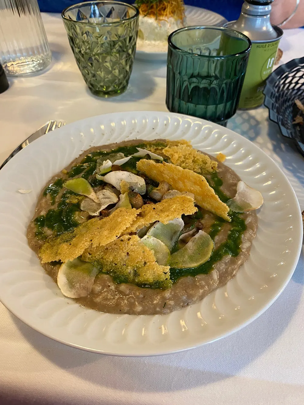 Plat de risotto aux champignons, huile d'herbes et tuiles de fromage, dans une assiette blanche à bord cannelé