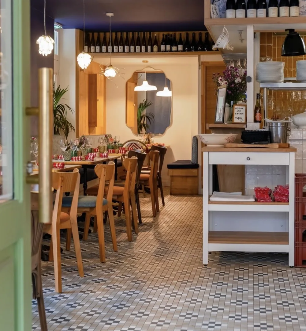 La salle : sol en carreaux à motifs, chaises en bois, étagères de bouteilles et carreaux jaunes au fond